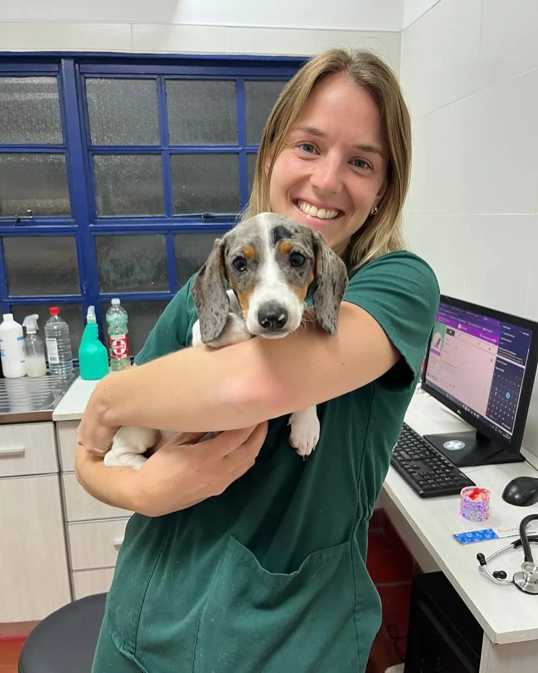 Jazmín, con ambo verde, sonríe con un cachorro salchicha en brazos